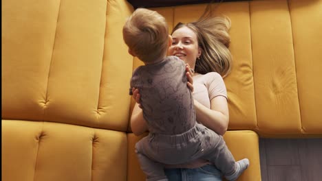 Woman-is-swinging-and-raising-kid-while-lying-on-couch,-top-view