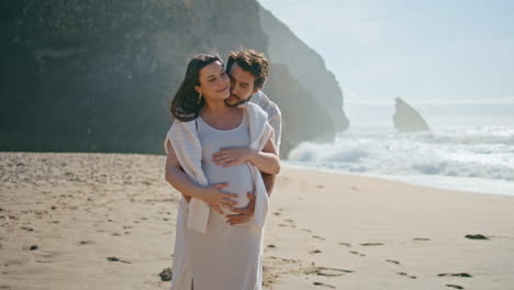 pareja embarazada abrazada caminando por la playa frente a las olas del océano. cónyuges esperando bebé