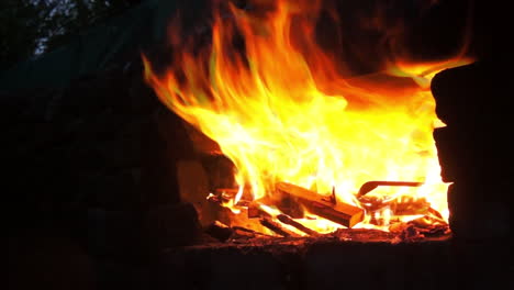 a wood fire producing aggressive flames built into a black rock - brick wall roars as the flames come out over the edge