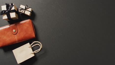 leather purse, gift bag and gift boxes with black ribbons on black background with copy space