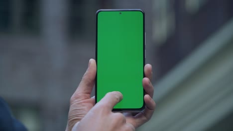 4k close-up of man's hand holding smartphone with green screen on street in city