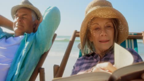 front view of active senior caucasian woman reading a book on the beach 4k