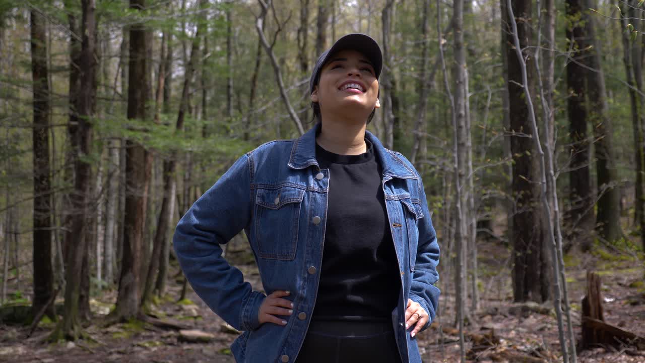 Young and pretty spanish woman smiling big and enjoying sunshine outdoors on hiking trail in upstate new york