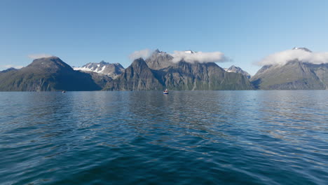 vista cinematográfica del paisaje noruego en un día de verano con un barco pesquero en el fiordo de lyngen y las montañas rocosas de los alpes escandinavos al fondo, noruega