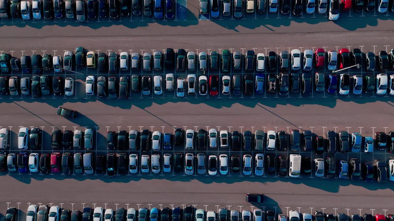 Dronebillede fra oven af en overfyldt udendørs parkeringsplads, der viser biler, der kører ind, cirkulerer og parkerer under en typisk morgenmyldretid