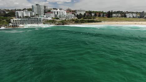 surfers surfing on surfboards on seawater with bondi icebergs swimming club in background, australia