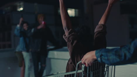 happy group of friends playing with shopping cart having fun on rooftop at night enjoying weekend celebration party