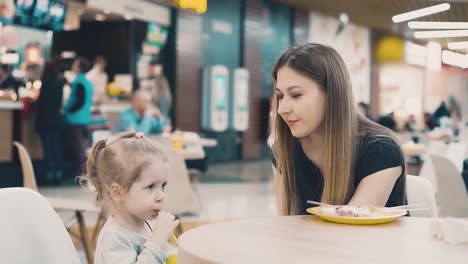 young beautiful mother with her little daughter sitting in a cafe mom gives her daughter a drink through straw