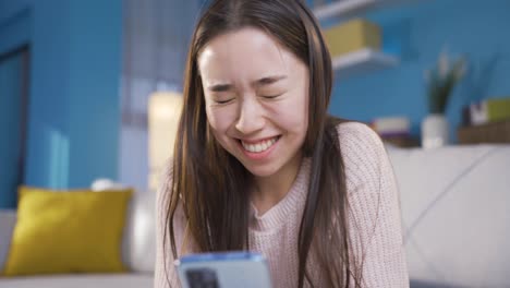스마트폰을 들고 있는 행복한 젊은 여성이 휴대폰 화면에서 웃으며 재미를 느끼고 있습니다.