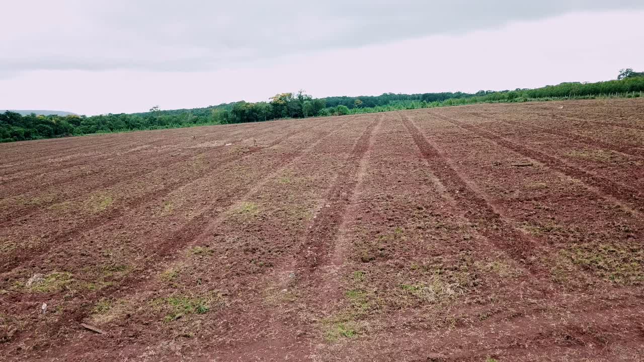 Vista expansiva de un paisaje rural con un gran campo arado. Hierba verde crece en el suelo fértil bajo un cielo nublado.
