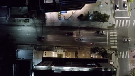 Descending-aerial-drone-bird's-eye-top-shot-of-a-small-street-intersection-surrounded-by-apartments-in-the-tropical-beach-capital-city-of-Joao-Pessoa,-Paraiba,-Brazil-during-a-warm-summer-night