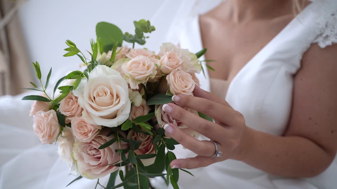 Sposa elegante in abito bianco che tiene un bouquet nuziale di rose e indossa un anello di diamanti, slow motion.