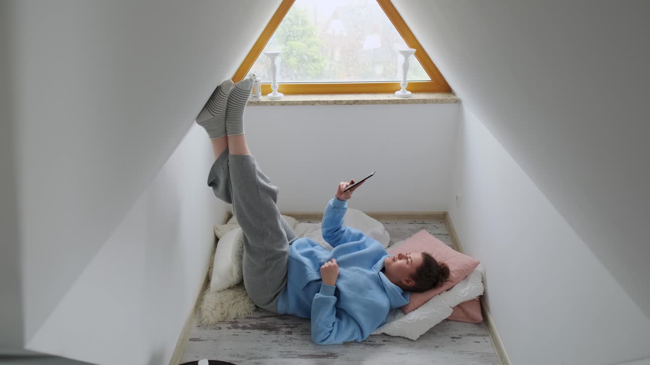 Woman Relaxing in Attic Room with Phone