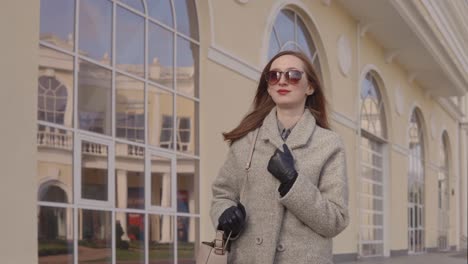 woman in a beige coat walking outside a modern building