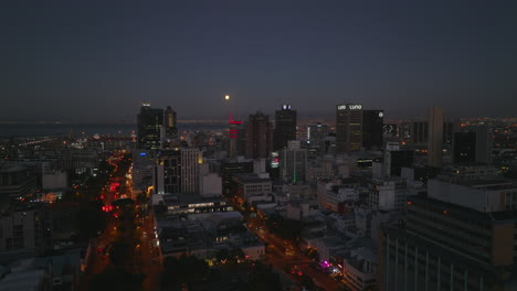 Aufsteigende-Aufnahme-Des-Stadtzentrums-Bei-Nacht.-Beleuchtete-Straßen-Und-Hochhäuser.-Aufschlussreiche-Meeresbucht-Mit-Seehafen.-Kapstadt,-Süd-Afrika