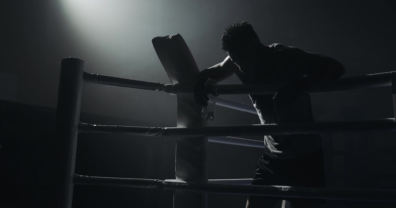 Silhouette of a Tired Boxer Resting in a Dark Boxing Ring