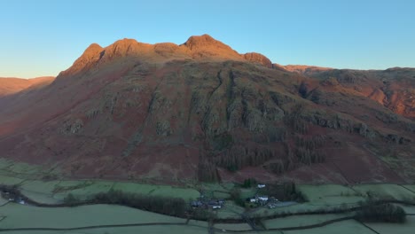 flight over shadowy valley up towards mountain peaks catching winter dawn light. langdale pikes, english lake district, cumbria, uk.