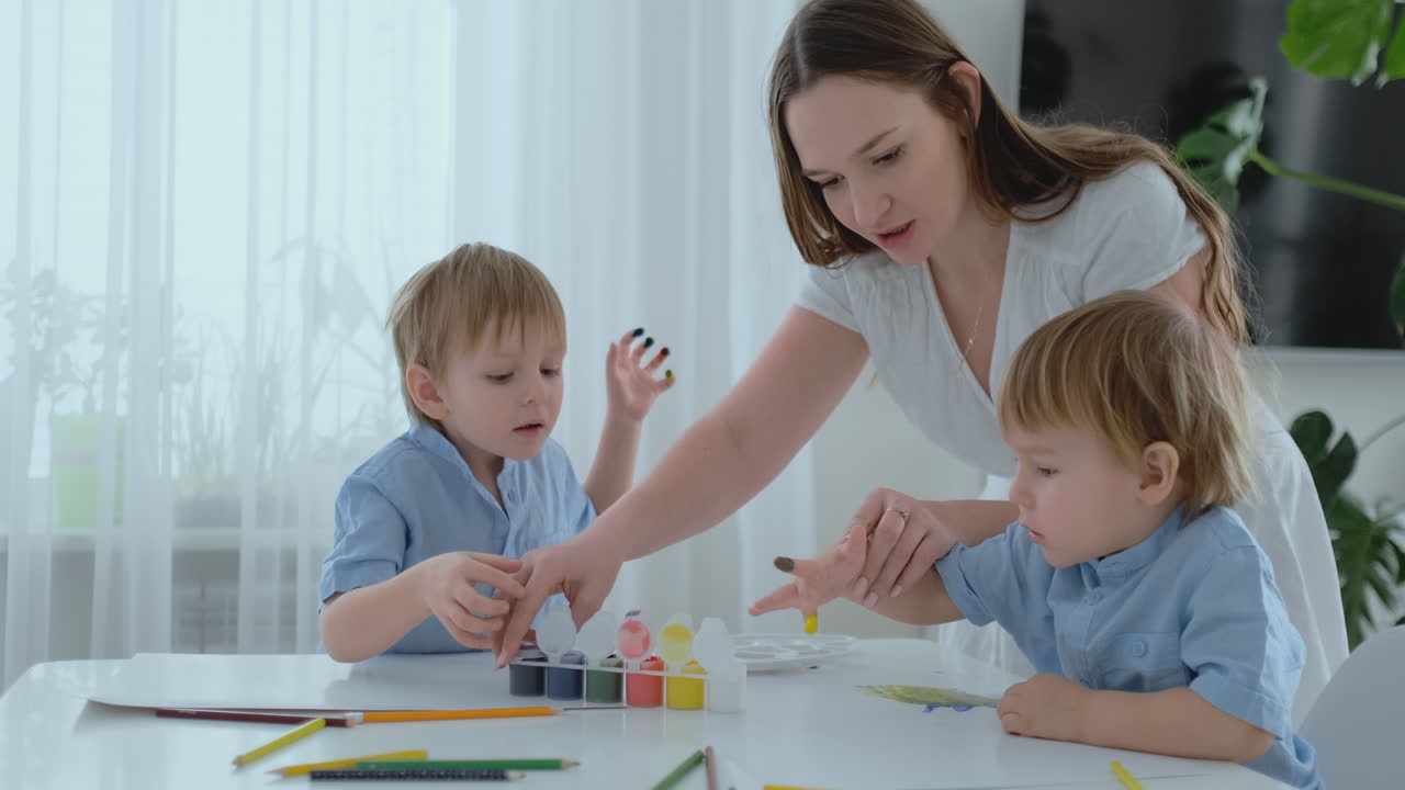 Mom helps her sons to develop creative skills and is engaged with them to create drawing paints with the help of fingers. Child development. Creative family. Loving mom