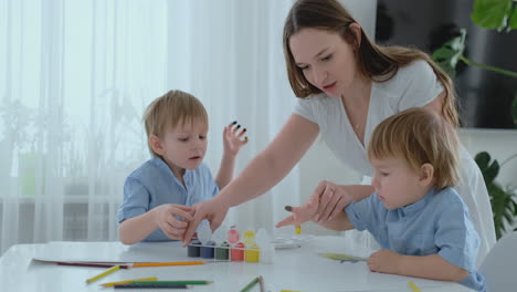 Mom-helps-her-sons-to-develop-creative-skills-and-is-engaged-with-them-to-create-drawing-paints-with-the-help-of-fingers.-Child-development.-Creative-family.-Loving-mom