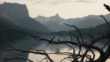 lago escondido y las montañas rocosas de montana vistas a través de ramas sin hojas, parque nacional de glaciares