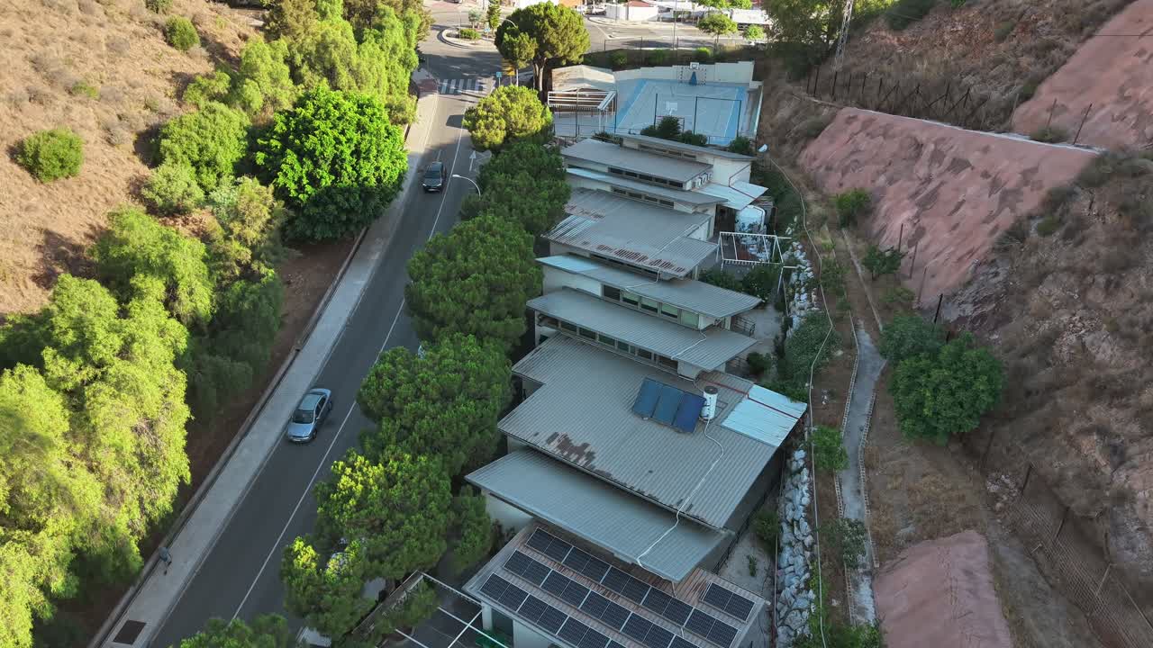 An aerial drone shot captures modern, terraced homes with multiple solar panels on a hillside in Vicente Paul, Spain. This highlights a concept of sustainable architecture and urban living