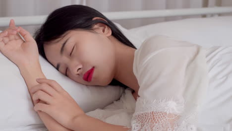 피자마를 입고 일어나는 아름다운 소녀의 실제, 큰 창문 근처에 앉아있는 침대에서 깨어나는, 완전히 휴식을 취하고, 아침에 신선한 공기와 빛을 얻기 위해 커튼을 펴는.