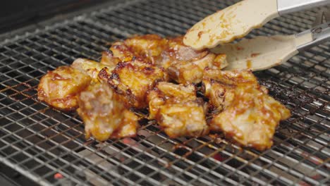 fotografía de cerca de costillas de cerdo, carne agarrada con pinzas en la parrilla por un cocinero