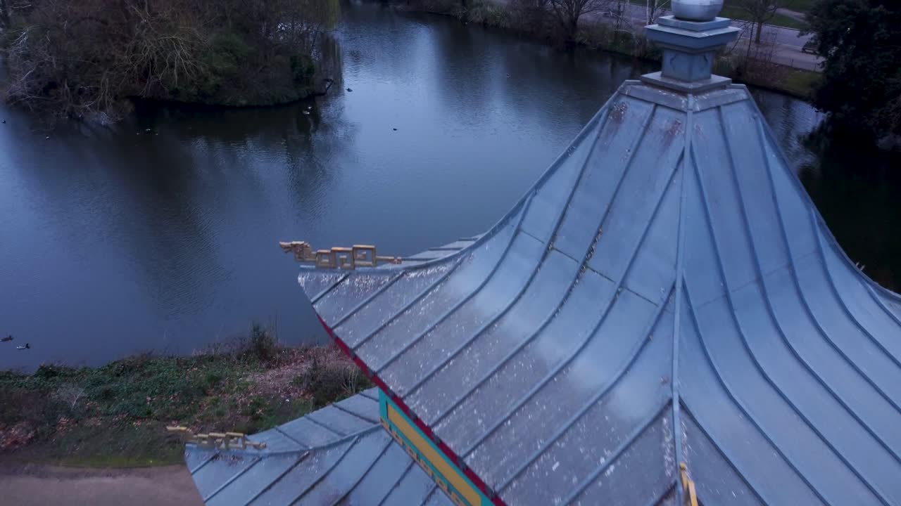 En låg flygvy över en parkpagod och damm i östra London. Filmat tidigt på morgonen med en cirkulerande rörelse runt Victoria Park Pagoda