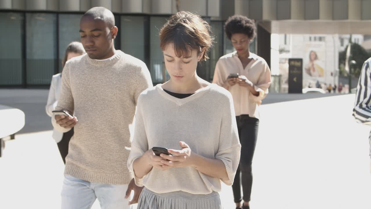 Front view of young citizens walking on street with phones