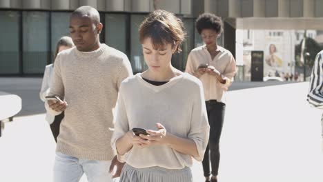 Front-view-of-young-citizens-walking-on-street-with-phones