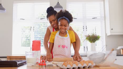 Front-view-of-mid-adult-black-mother-and-daughter-rolling-dough-in-kitchen-of-comfortable-home-4k