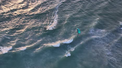 Vogelperspektive-Eines-Kitesurfers-Bei-Sonnenuntergang,-Der-über-Weiße-Wellen-Segelt,-Mit-Wunderschönem-Sonnenlicht,-Das-Sanft-Vom-Wasser-Reflektiert-Wird