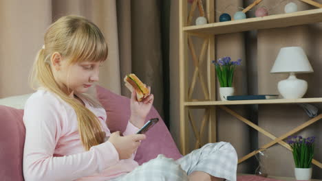 Mädchen-Benutzt-Smartphone-Und-Hat-Ein-Sandwich-In-Ihrem-Schlafzimmer