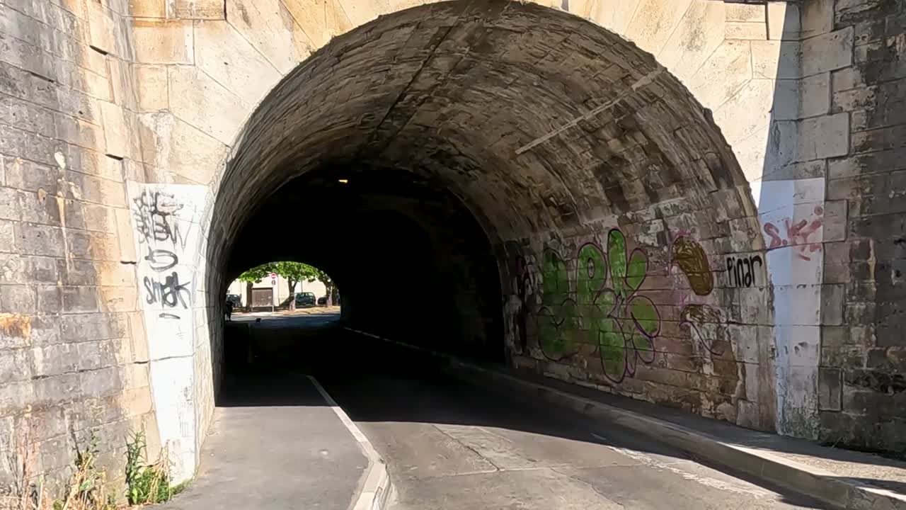 A stone tunnel featuring vibrant graffiti and a paved road, illuminated by natural light.