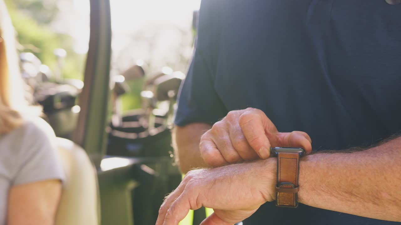 cerca del hombre comprobando reloj inteligente como una pareja madura sentarse en el buggy y jugar una ronda de golf juntos