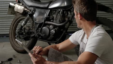 male mechanic using digital tablet in motorbike repair garage 4k