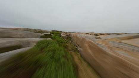 fpv drone flying fast and low over a rocky terrain of ramsvik shoreline in sweden