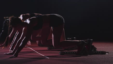 three girls in black clothes are in the starting pads to start the race in the competition in the light of the lights and run towards the finish