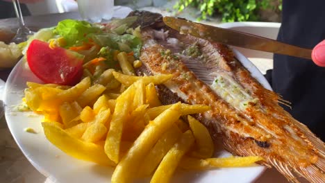 Comiendo-Una-Lubina-A-La-Parrilla-Con-Papas-Fritas-Y-Ensalada,-Comida-Tradicional-Española-En-Un-Restaurante,-Toma-De-4k