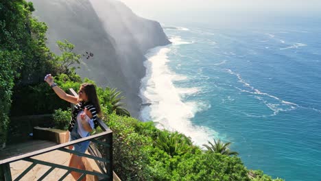 una joven turista toma fotos con su teléfono móvil en el mirador de un acantilado con vista al océano en tenerife, islas canarias