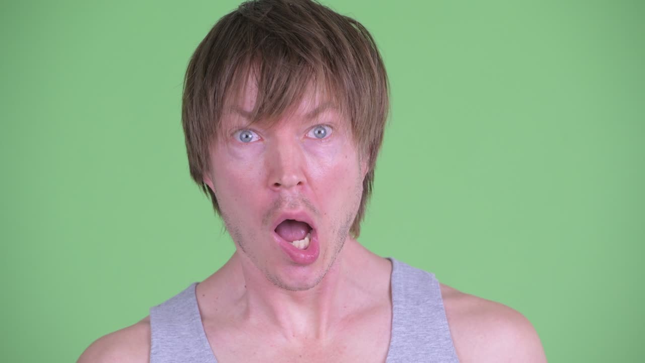 zoom en retrato de un hombre caucásico mirando conmocionado y sorprendido disparado contra el fondo verde del estudio