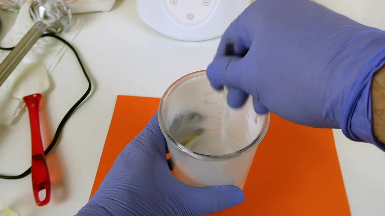 Mani guantate che mescolano accuratamente polvere bianca e liquido giallo in un becher di vetro per creare cosmetici
