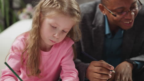 Niña-Dibuja-En-La-Educación-En-Casa-Con-Un-Maestro-Afroamericano