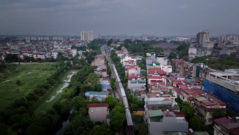 drone dolly above a train moving through central hanoi, vietnam, with an aerial establishing view of the city skyline and railway