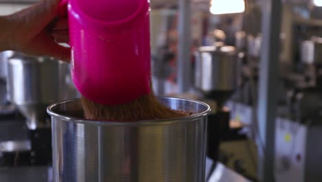 Close-up-of-a-hand-pouring-a-bag-of-nuts-in-a-big-container-in-a-factory