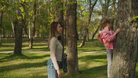 Mother-stands-near-daughter-studying-tree-rough-bark-in-park