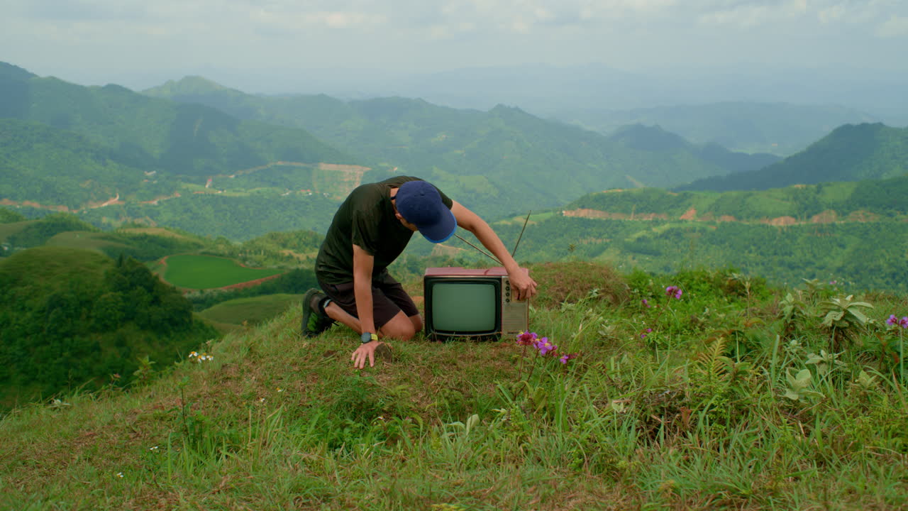 un hombre curioso inspecciona un televisor en la ladera de una montaña