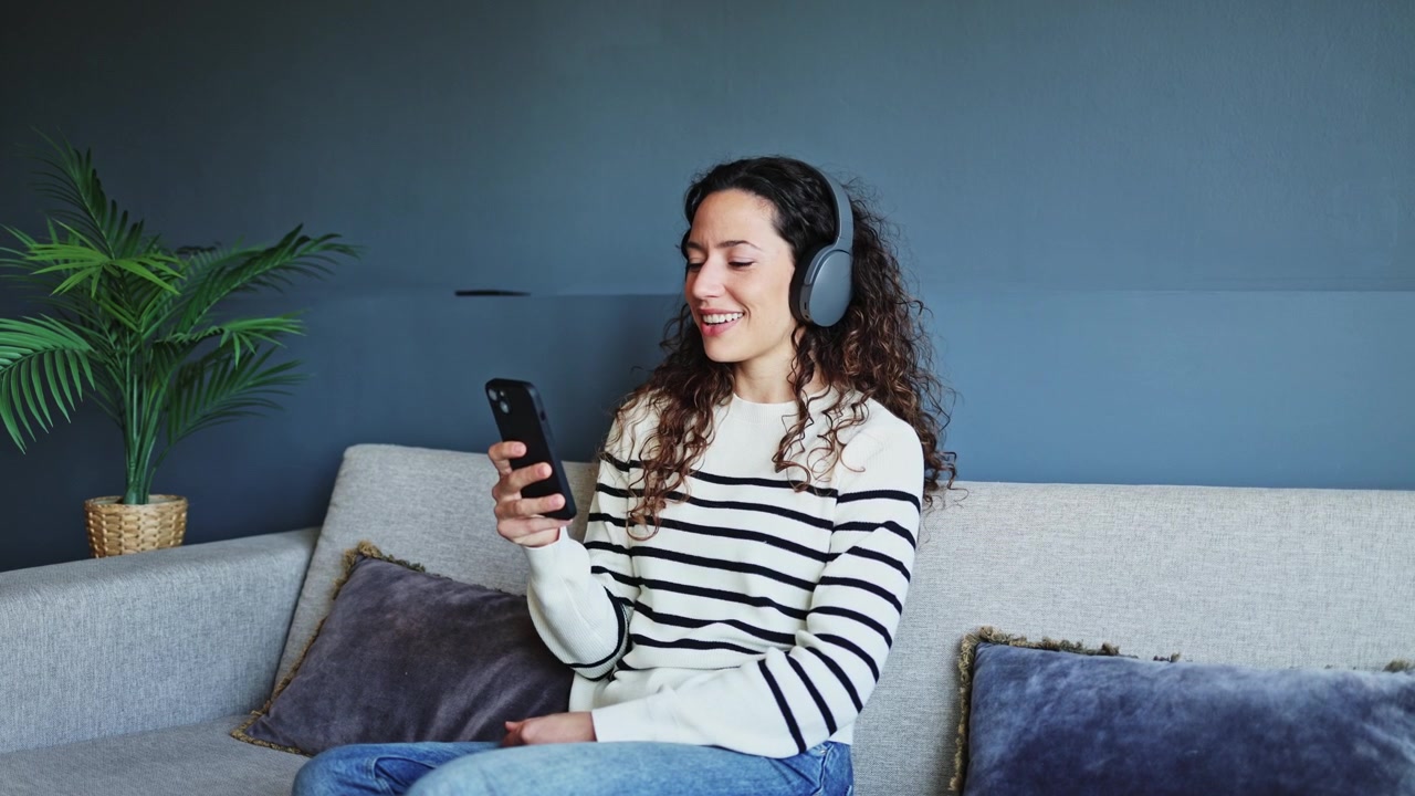 Giovane Donna con le Cuffie che Usa lo Smartphone sul Divano