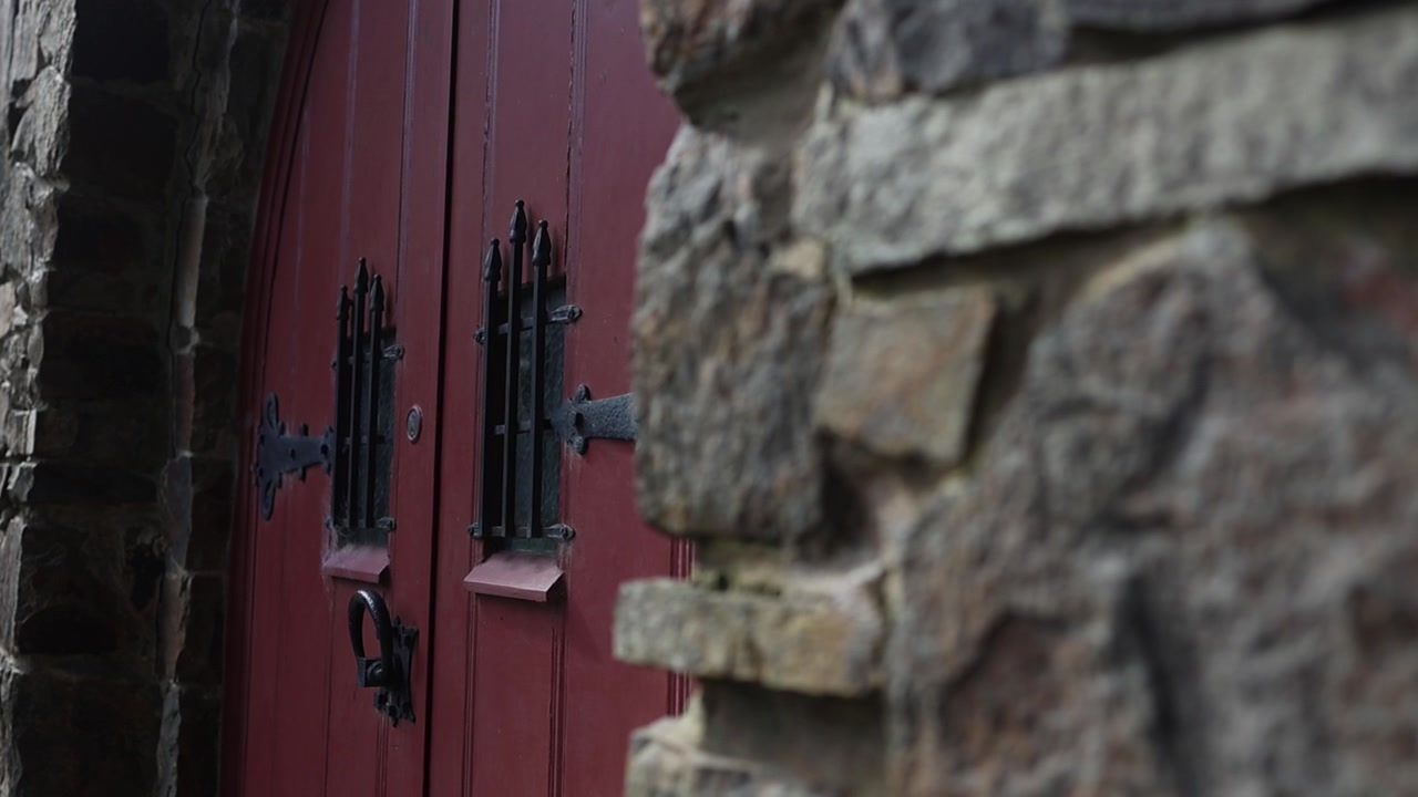 Olinda, Melbourne'de eski bir taş kilise girişinin yakın çekimi. Siyah ferforje detaylı kırmızı ahşap kapılar, loş doğal ışık, sığ alan derinliği ve dokulu duvar işçiliği.