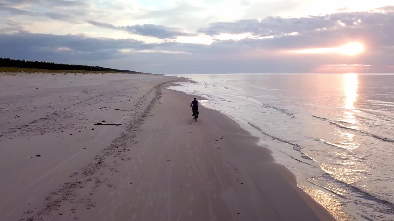해질녘 해변에서 자전거를 타는 청년의 슬로모션 항공 샷